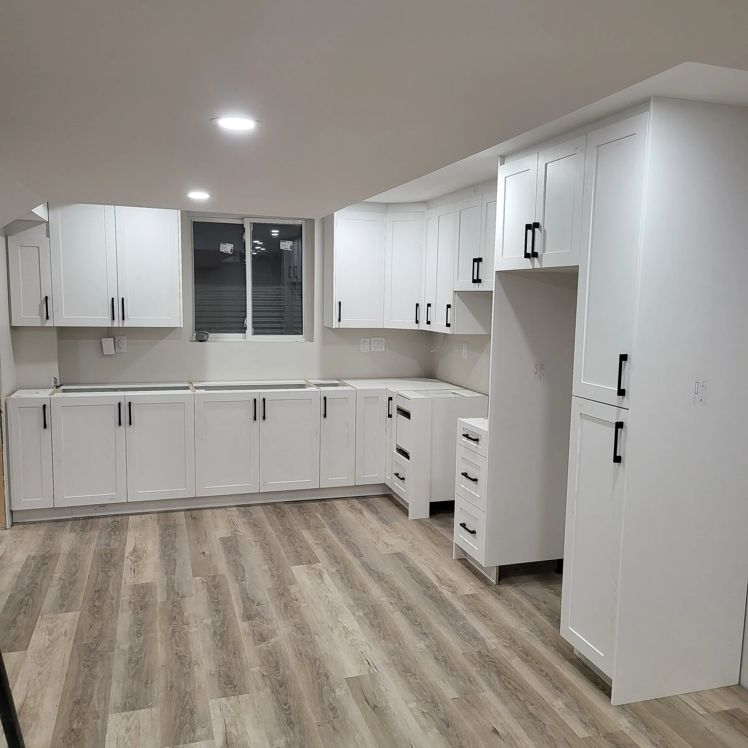 Finished basement kitchenette with white shaker cabinetry, black hardware, quartz counter and vinyl plank flooring