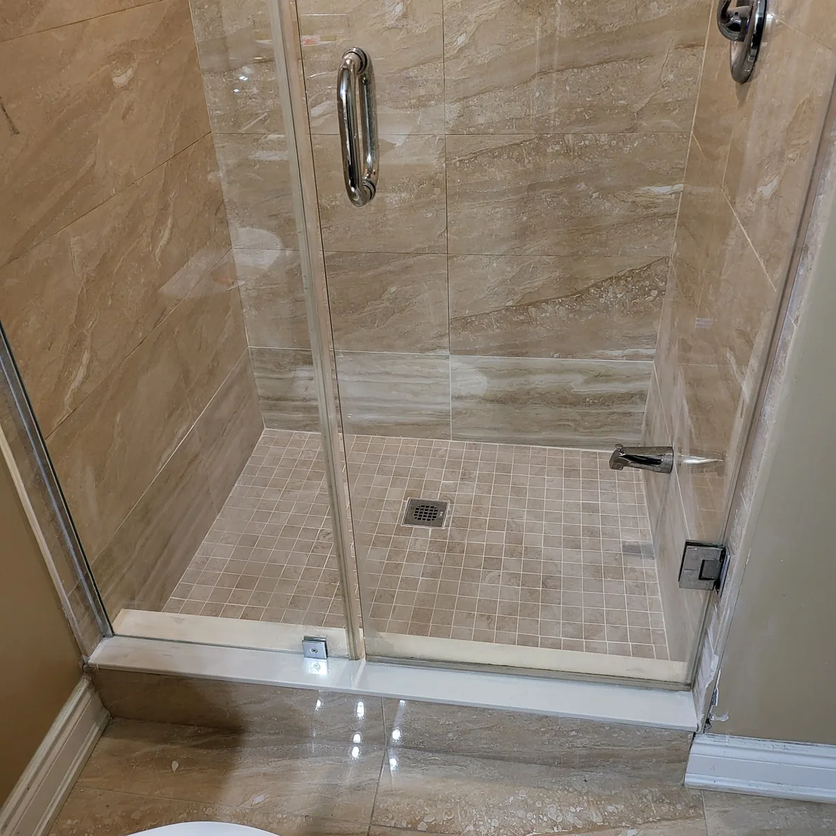 Finished walk-in shower tiled in stone-look porcelain with a mosaic floor, chrome fixtures and a framed glass door