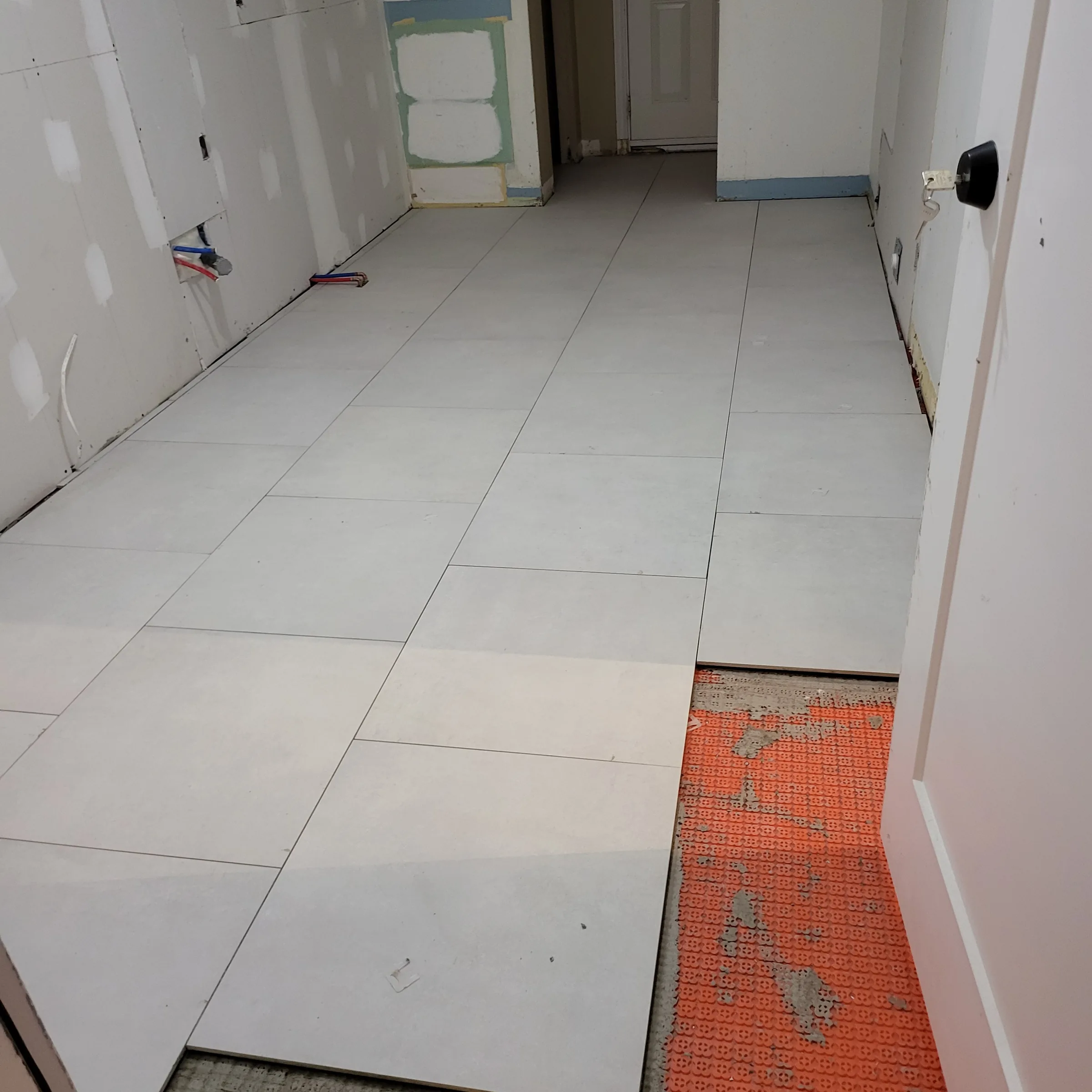 Large-format floor tile being set over an orange uncoupling membrane during a renovation