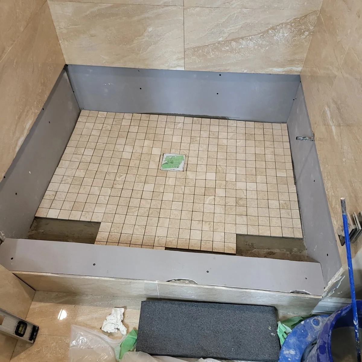 Mosaic tile being set into a shower pan, with the surrounding walls already tiled