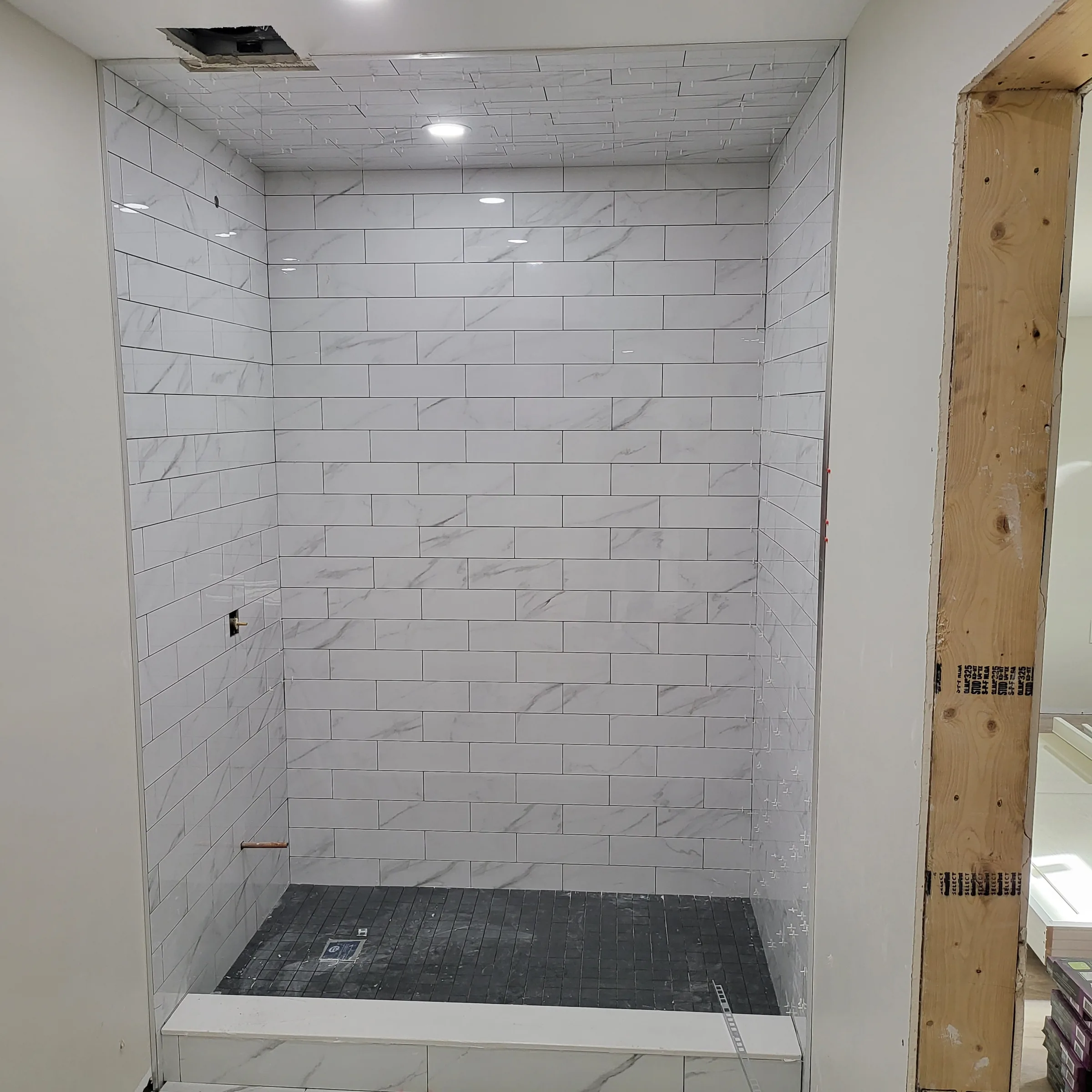 Shower surround tiled in marble-look subway tile, photographed before the pan and fixtures were finished